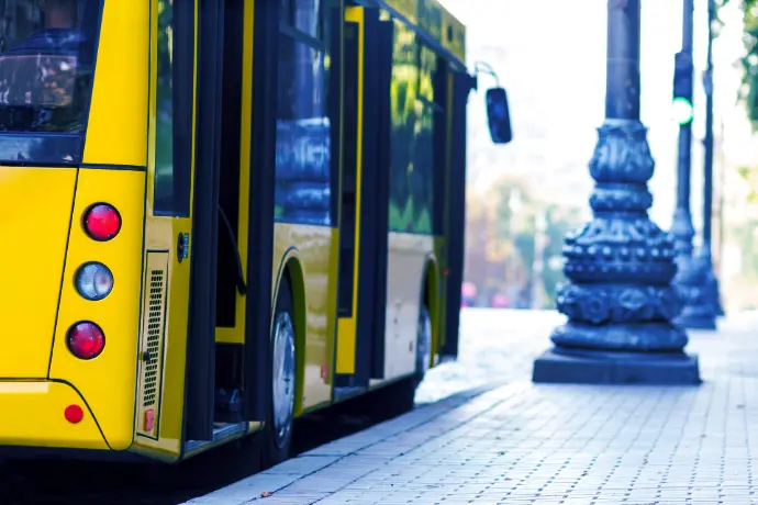 Close-up van een gele stadsbus bij een halte met wazige passagiers op de achtergrond