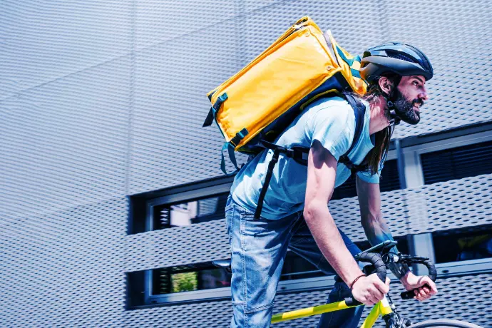 Bezorger op de fiets met een gele rugzak in een stedelijke omgeving