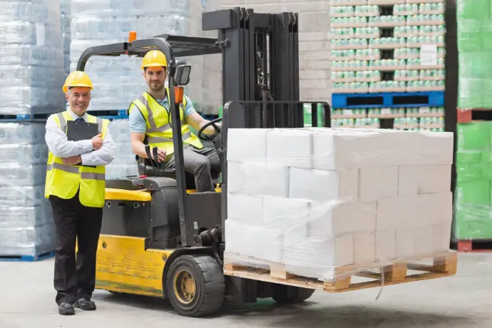 Warehouse worker operating a forklift while another checks inventory