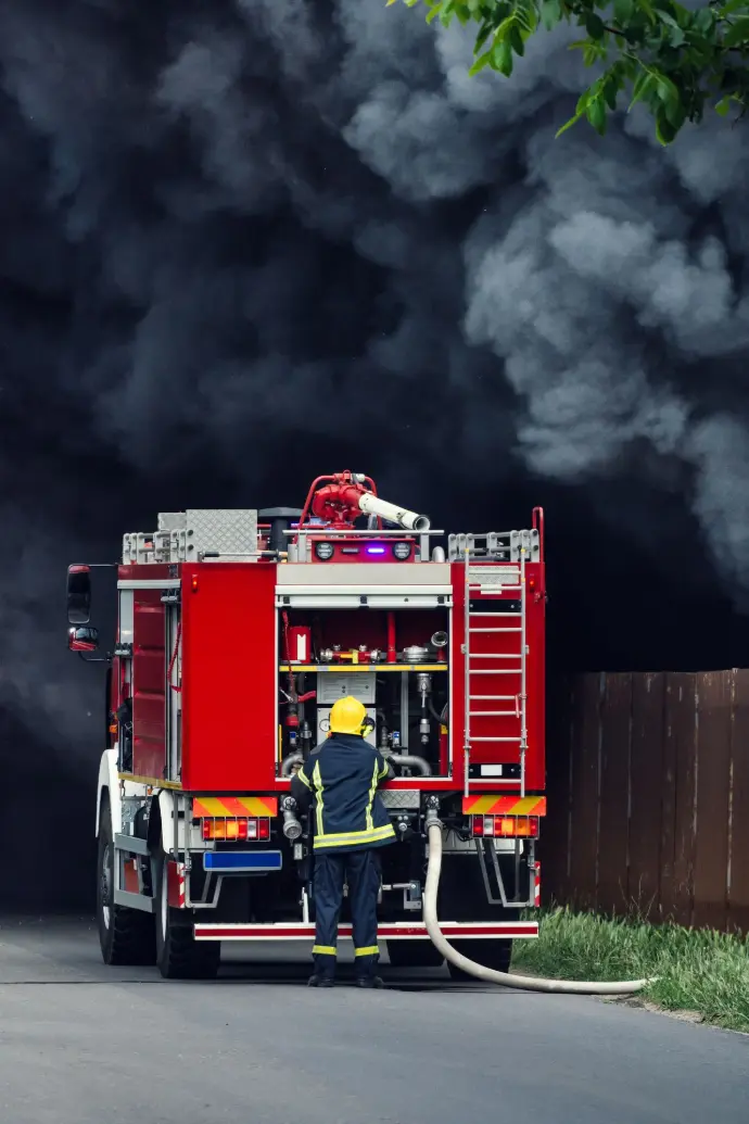 Firefighter operating at the rear of a fire truck with dark smoke in the background